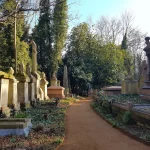 Path running next to gravestones lit up by sunlight in Highgate Cemetery in London