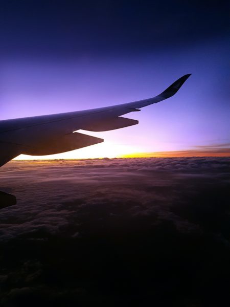 View from the plane window. Plane wings, purple sky, and clouds with a yellow hue. Just one of many things to expect on a long haul flight.