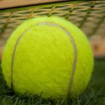 Close up of tennis ball laying on tennis court with racquet in background