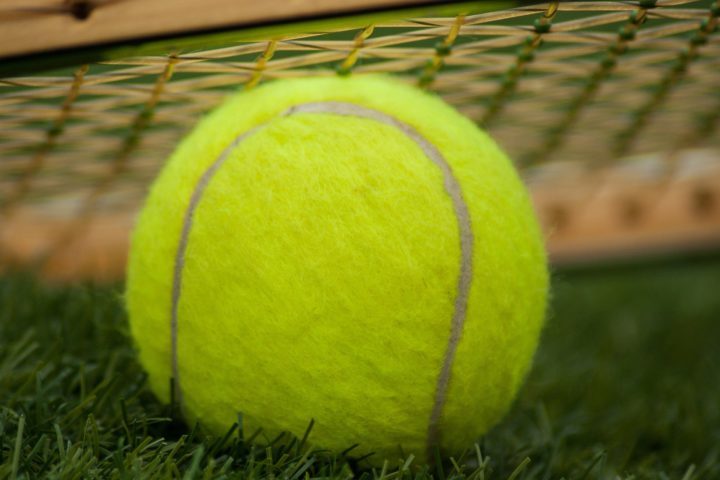 Close up of tennis ball laying on tennis court with racquet in background