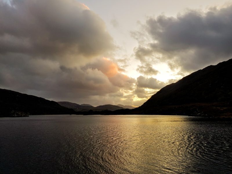 A late afternoon view of a large body of water with the sun setting behind clouds