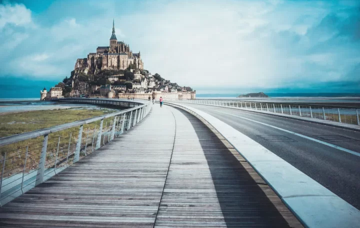 View of Mont-Saint Michel from a distance with walkway in centre image. Just one of many amazing cities to explore in Normandy