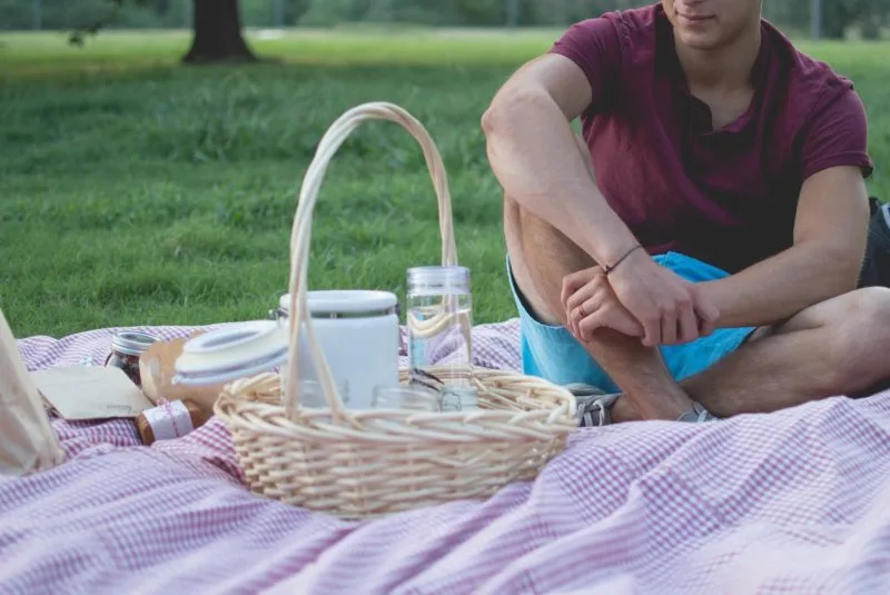 Man sitting on picnic rug in park. A picnic in the park is one of our favourite romantic things to do in London