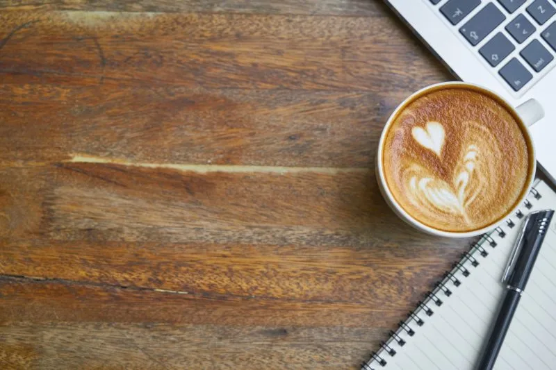 Coffee cup on table next to laptop and notepad