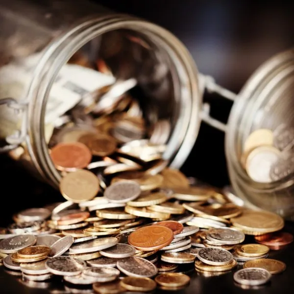 Jar of pennies laying on side with coins spilling out on table. 