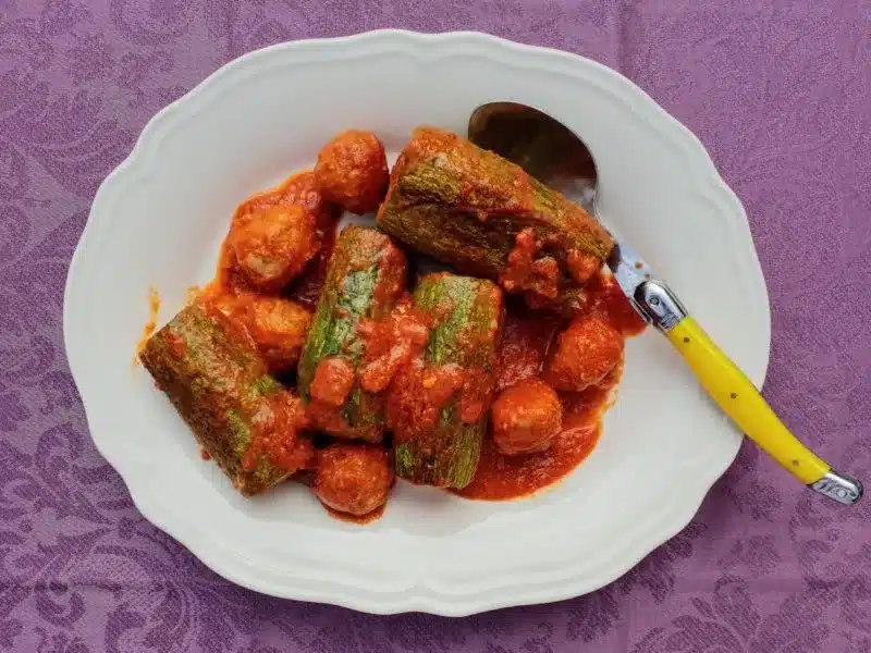 Homemade stuffed zucchini on a white plate on purple tablecloth 