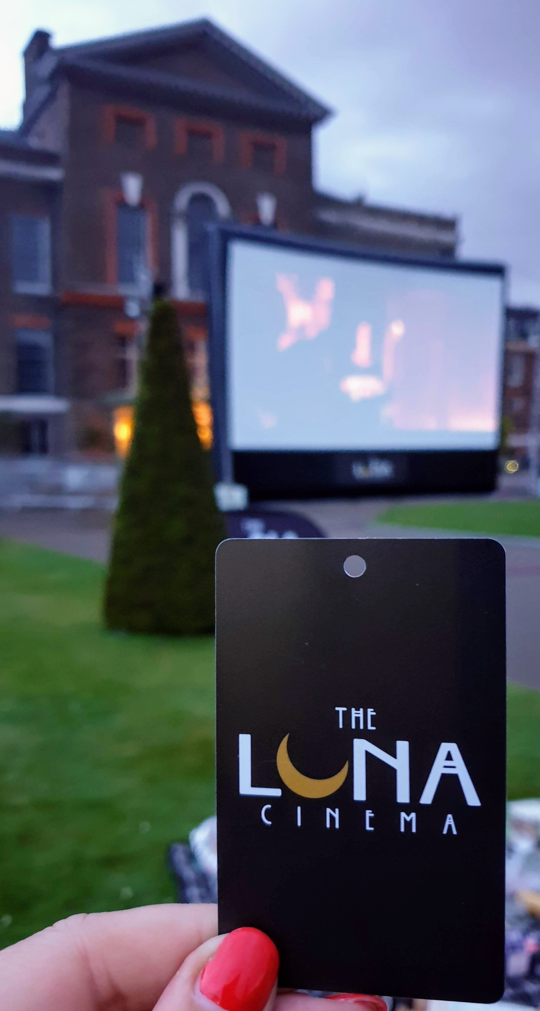 Luna Cinema ticket held up against background of the large screen at Kensington Palace