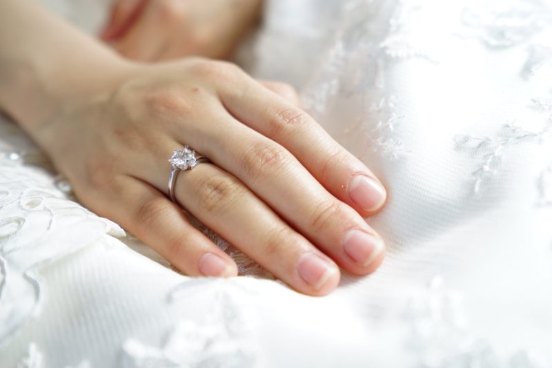 Hand wearing an engagement ring on a white sheet
