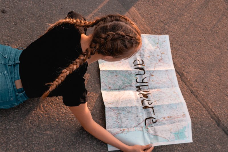 Shot over the shoulder of a girl reading a map which says anywhere in text over the map