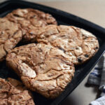 Chocolate chip cookies laying on a charcoal baking tray on a timber surface