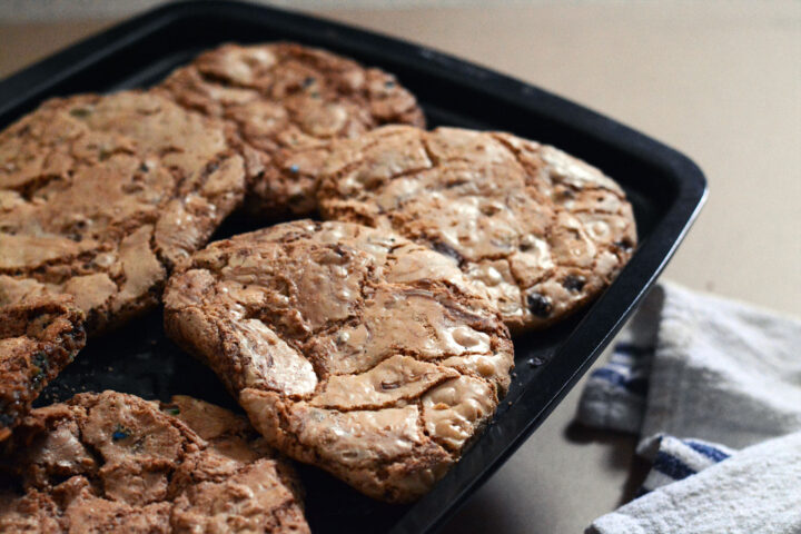 Chocolate chip cookies laying on a charcoal baking tray on a timber surface