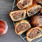 Australian sausage roll on a metal plate with a jar of ketchup (tomato sauce)