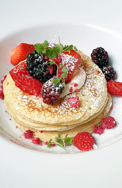 Pancakes on a white plate topped with red berries