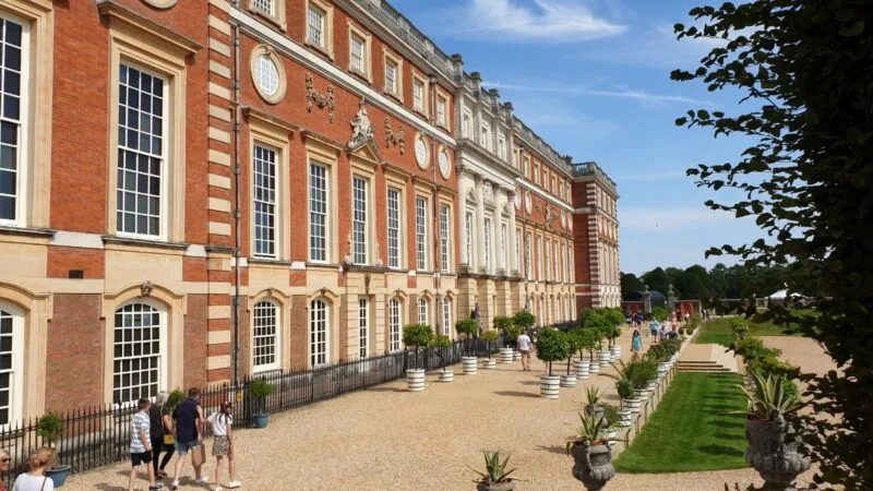 For a Day Trip from London try Hampton Court Palace. Exterior of building with cream-coloured pebble path outside. Just one of many places to include on this list of car day trips from London
