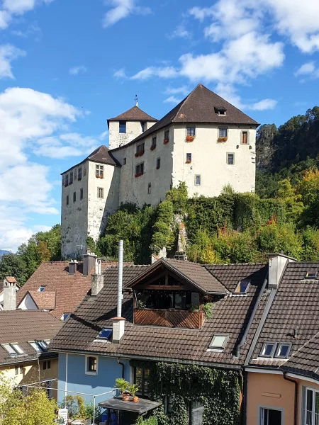 Schattenburg Castle sitting high on a hill above residential houses. Blue sky in the background. Just one of many things to do in Feldkirch Austria. 