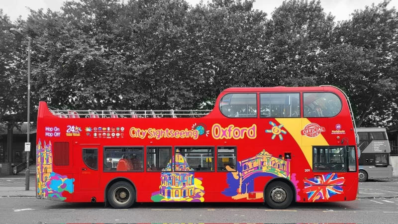 A bright red City Sightseeing Oxford Tour bus sert against a black and white background. Just one of the many things to do in Oxford in a day.