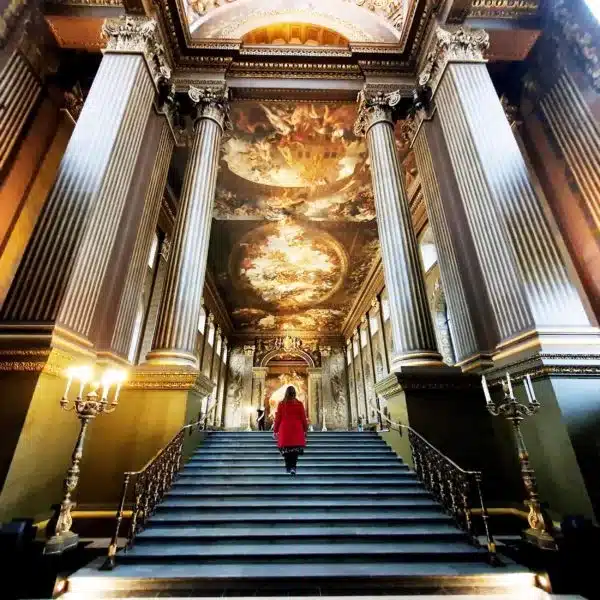Roma in a red coat walking up the stairs in the Painted Hall in Greenwich