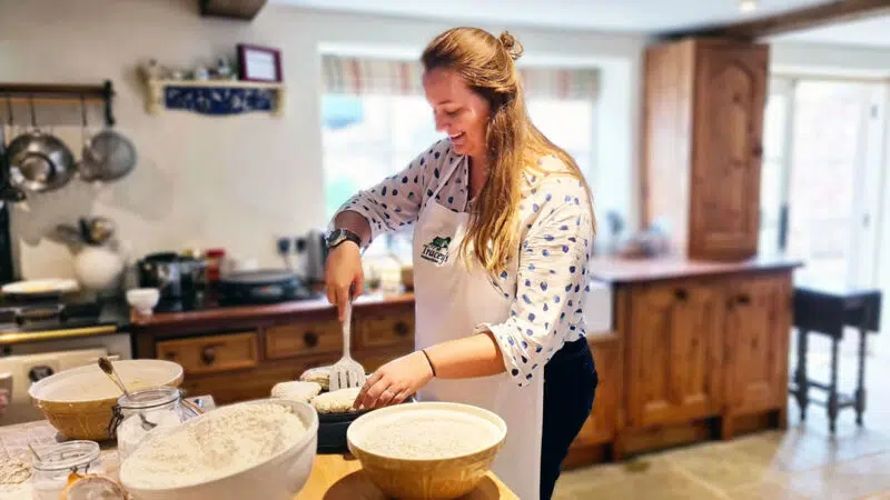 Roma wearing a white apron, holding a spatula trying to flip Irish bread on a griddle