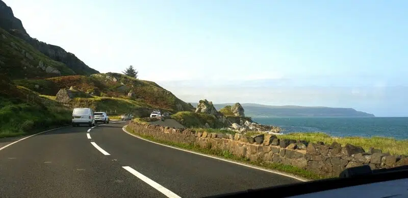 Road winding through the Causeway Coastal Route. Visible is ocean, a road curving ahead, and cars coming towards.