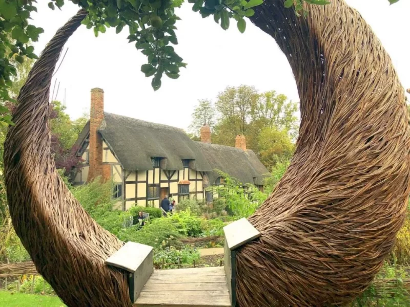 Sculpture made from natural vines and branches in the foreground and thatched-roof building in the middle of photo. Just one of many places for a day trip from London.