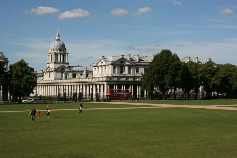View of the Greenwich Old Royal Naval College taken from a distance to showcase the green grass and blue skies