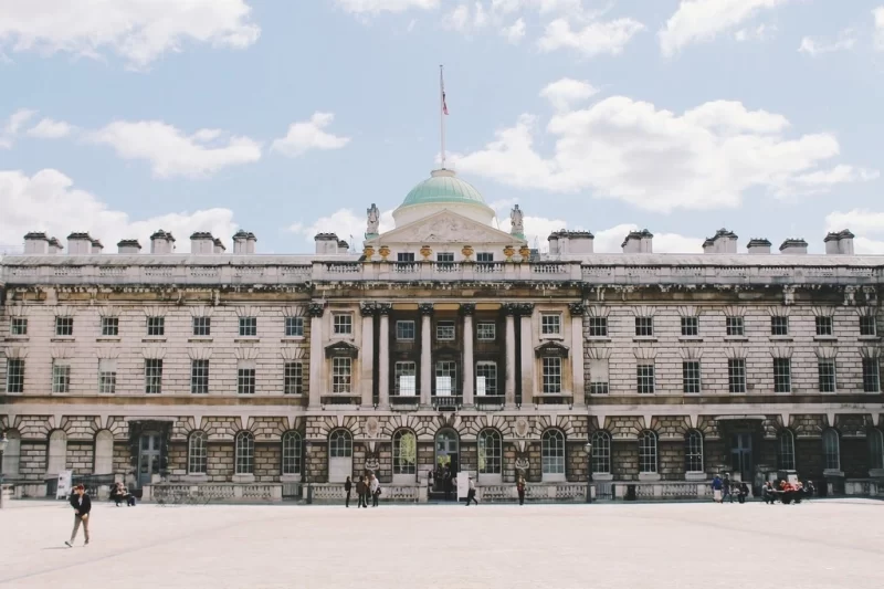 Exterior view of the internal courtyard Somerset House. The courtyard is relatively empty with only some people visible and a sky blue sky in the background. 