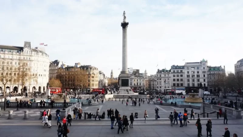 Wide angled view of Trafalgar Square on a bright day with crowds of people exploring this London landmark to visit