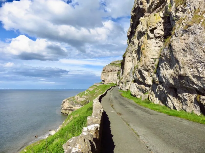 Empty road with a high cliff face on he right and the sea on the left