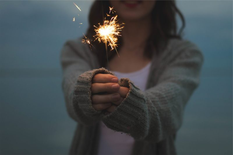 Woman standing with arms outstretched holding a sparkler